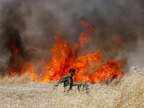 An Israeli soldier attempts to extinguish a fire in a wheat field near the Kibbutz of Nahal Oz, along the border with the Gaza strip, on May 14, 2018 after it was caused by incendiaries tied to kites flown by Palestinian protesters from across the border.