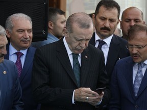 FILE - In this Friday, May 4, 2018 file photo, Turkey's President Recep Tayyip Erdogan, center, looks at his phone during a ceremony for the re-opening of the Spice Bazaar following restoration in Istanbul. The Turkish lira has lost more than 20 percent of its value against the dollar since the start of the year, hurting many in the country, especially small business owners who rely on imported machinery and goods.