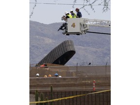 Investigators look down at a toppled crane that was being used in the construction of the Sky Train guideway system at Sky Harbor International Airport Monday, May 21, 2018, in Phoenix. The Phoenix fire department said one person is unaccounted for and their condition is unknown at this time due to the crane being on its side.