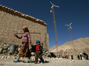 A Uighur woman walks past wind turbines with her son to fetch water in the remote Bulunkou township in the mountains south of Kashgar, Xinjinag.