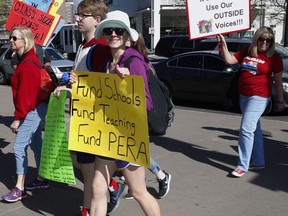 In this April 27, 2018, photograph, a teacher carries a placed in support of funding the state employee pension fund that teachers belong to during a rally in Denver. Rising pension costs are eating away at teacher pay in Colorado and other states. The pension issue has played a role in a teacher uprising sweeping the U.S. Thousands of Colorado teachers walked off the job and closed down schools last week.
