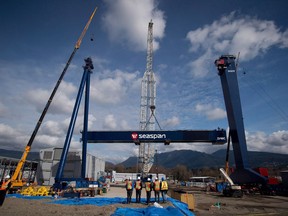 Workers watch as the main girder of a new 300-tonne gantry crane is lifted into place at Seaspan Vancouver Shipyards in North Vancouver, B.C., on Wednesday April 2, 2014. The federal government is greenlighting plans to start some work on the navy's new support ships in the coming months in a bid to keep delivery the much-needed vessels from slipping farther behind schedule.