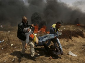 File - In this Friday, April 27, 2018 file photo, Palestinian protesters evacuate a wounded youth during a protest at the Gaza Strip's border with Israel, east of Khan Younis. The deadly scenes that have been playing out for weeks now along Gaza's border, with thousands of Palestinians marching and threatening to storm the security fence and Israeli troops opening fire, are eerily familiar to Israeli author Mishka Ben-David. They have already taken place _ on the pages of his best-selling thriller last year, "The Shark." And while the novel's doomsday scenario may seem far-fetched to some, Ben-David fears for the region in the absence of an overall peace initiative.