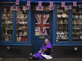 A woman sits at the door of a closed souvenirs shop, near Windsor castle, England, Friday, May 18, 2018. Preparations continue in Windsor ahead of the royal wedding of Britain's Prince Harry and Meghan Markle Saturday, May 19.