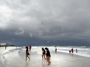 Beachgoers walk on Okaloosa Island in Fort Walton Beach, Fla., Monday, May 28, 2018, as Subtropical Storm Alberto approaches the Gulf Coast. The storm's gusty rain and brisk winds roiled the seas near the U.S. Gulf Coast on Monday, keeping white sandy beaches emptied of their usual Memorial Day crowds.