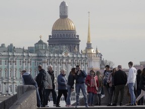 In this photo taken on Thursday, May 3, 2018, people walk at the Neva River embankment in St. Petersburg, Russia, with the city landmarks, Zimny (Winter) palace, Admiralty building and St. Isaac's Cathedral in the background.