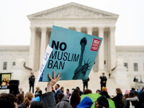 FILE - In this April 25, 2018 file photo, a person holds up a sign that reads "No Muslim Ban" during an anti-Muslim ban rally as the Supreme Court hears arguments about wether President Donald Trump's ban on travelers from several mostly Muslim countries violates immigration law or the Constitution in Washington. A review by The Associated Press of decisions by nearly 40 federal district court and appellate judges on President Donald Trump's various travel bans shows a sharp divide between judges nominated by Republicans and those nominated by Democrats.