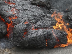 Lava burns across a road in the Leilani Estates subdivision on Saturday, May 5, 2018, near Pahoa, Hawaii. Glowing plumes of lava have shot hundreds of feet into the air at points, officials said, and black-and-orange ribbons of rock have curled into roadways.