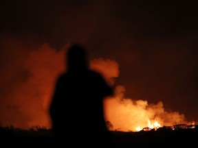 A man photographs lava erupting from from a fissure near Pahoa, Hawaii Saturday, May 19, 2018. Two fissures that opened up in a rural Hawaii community have merged to produce faster and more fluid lava. Scientists say the characteristics of lava oozing from fissures in the ground has changed significantly as new magma mixes with decades-old stored lava.