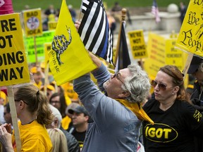 FILE - In this April 25, 2018 file photo, Dave Fitzgerald of Girard, Ill. waves flags while  listening to speakers during the annual IGOLD (Illinois Gun Owners Lobby Day) rally at the Capitol 8 in Springfield, Ill. A growing number of rural counties in Illinois are standing up for their rights as gun owners and to do it they've co-opted a word that to conservatives represents nothing more than a liberal policy to skirt the law: Sanctuary. (Rich Saal/The State Journal-Register via AP File)/