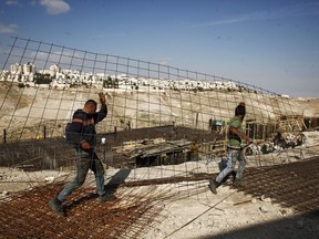 FILE - In this Jan. 22, 2017 file photo, workers carry material at a construction site in the West Bank settlement of Maaleh Adumim. Israeli Defense Minister Avigdor Lieberman said Thursday, May 24, 2018, that he will seek approval next week to fast-track construction of 2,500 new West Bank settlement homes this year and advance 1,400 more units that are currently in the planning stage. Senior Palestinian official Hanan Ashrawi condemned Lieberman's announcement as "Israeli colonialism, expansionism and lawlessness" and called on the International Criminal Court in The Hague, Netherlands, to launch an investigation.