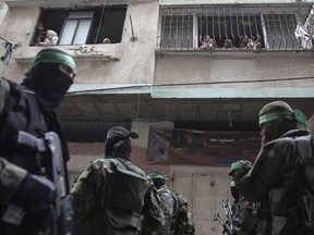 Palestinians look from their windows as masked Hamas gunmen attend a funeral for six Hamas fighters who were killed in an explosion Saturday, in Deir el-Balah, central Gaza Strip, Sunday, May 6, 2018. Hamas is vowing revenge after blaming Israel for the explosion.