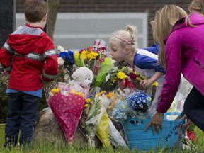 A girl leans over bouquets of flowers to blow a kiss at a memorial in front of East Brook Middle School, Friday, May 18, 2018, in Paramus, N.J. Investigators are combing through evidence seeking answers to why a school bus carrying 45 fifth-graders and teachers on a field trip collided with a dump truck on Thursday on a New Jersey highway, killing a student and teacher and sending dozens to area hospitals.