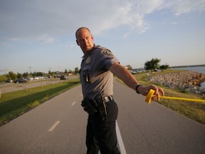 A policeman puts up crime scene tape around the scene of a shooting on the east side of Lake Hefner in Oklahoma City, Thursday, May 24, 2018. Police say a man armed with a pistol walked into an Oklahoma City restaurant and opened fire, wounding two people, before being shot dead by an armed civilian in the parking lot.