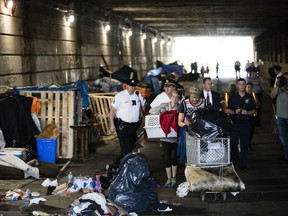 A couple, center, who were living under a bridge carry their possessions out as police move in to clear the encampment in Philadelphia, Wednesday, May 30, 2018.  The city's homeless packed up their few belongings as sanitation workers cleaned and power washed what had been a heroin encampment only moments before. The morning activity attended by police was part of a month-long pilot program meant to relocate addicts living under two bridges in Philadelphia.