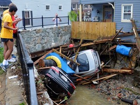 Residents gather by a bridge to look at cars left crumpled in one of the tributaries of the Patapsco River that burst its banks as it channeled through historic Main Street in Ellicott City, Md., Monday, May 28, 2018. Sunday's destructive flooding left the former mill town heartbroken as it had bounded back from another destructive storm less than two years ago.