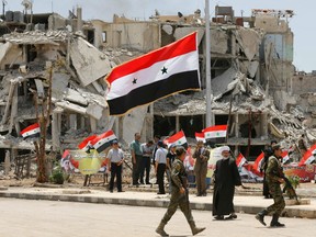 Pro-government force hold a portrait of the Syrian president during a flag raising ceremony at the entrance of the Hajar al-Aswad neighbourhood on the southern outskirts of the capital Damascus on May 24, 2018, after the regime seized the Yarmuk Palestinian camp and adjacent neighbourhoods of Tadamun and Hajar al-Aswad earlier in the week from the Islamic State (IS) group, putting Damascus fully under its control for the first time since 2012.