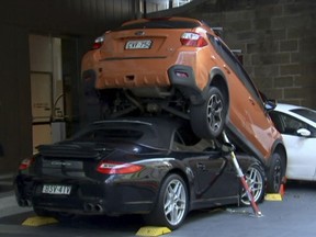 In this image made from video, a Porsche Carrera car is underneath another car in Sydney, Australia Thursday, May 31, 2018. Australian media say a valet drove the soft-top Porsche Carrera under another vehicle Thursday outside the Hyatt Regency Hotel in Sydney. (Australian Broadcasting Corp. via AP)