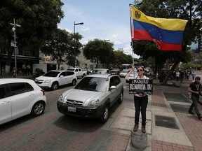 A demonstrator holds a Venezuelan flag and a placard that reads in Spanish: "Maduro, resign right now!” in Caracas, Venezuela, on May 23, 2018.