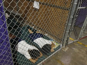 FILE - In this June 18, 2014 file photo, two female detainees sleep in a holding cell, as the children are separated by age group and gender, as hundreds of mostly Central American immigrant children are being processed and held at the U.S. Customs and Border Protection Nogales Placement Center in Nogales, Ariz.  President Donald Trump has seized on an error by liberal activists for tweeting photos of detainees at the U.S.-Mexico border in steel cages and blamed the current administration for separating immigrant children from their parents.  The photos were taken by The Associated Press in 2014, when President Barack Obama was in office.