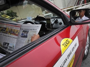 A taxi driver reads a newspaper reporting Mahathir Mohamad's sworn-in as Malaysia's new prime minister as he waits for customers in Kuala Lumpur, Malaysia, Friday, May 11, 2018. Malaysia's former authoritarian leader Mahathir was sworn in as prime minister on Thursday, cementing a stunning political comeback and a historic change in government after leading opposition parties to their first election victory in six decades.