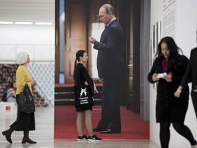 In this photo taken on Friday, May 4, 2018, visitors walk past a big photo of Russian President Vladimir Putin at a photo exhibition in Moscow, Russia. As Vladimir Putin begins his fourth term as Russia's president, his image is ubiquitous at home and effectively Russia's "brand" worldwide.