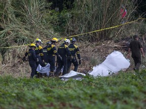 Firefighters carry a body bag that contains human remains recovered at the site where a Boeing 737 plummeted into a yuca field with more than 100 passengers on board, in Havana, Cuba, Friday, May 18, 2018. The Cuban airliner crashed just after takeoff from Havana's international airport in Havana, Cuba.