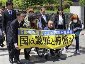 Kikuo Kojima, front third from left, a plaintiff who filed lawsuit against the government heads to the Sapporo district court in Sapporo, northern Japan Thursday, May 17, 2018. Three Japanese who were forcibly sterilized under a government policy decades ago have filed lawsuits demanding apology and compensation, in a movement growing across the country. The banner in Japanese reads " Government to apologize and compensate! "