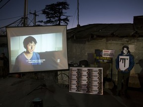 FILE - In this Jan. 8, 2018, file photo, an exile Tibetan wearing a mask in the likeness of 32-year-old Tashi Wangchuk, stands next to a screen projecting a New York Times video during a street protest demanding his release, in Dharmsala, India. China has sentenced the Tibetan language activist to five years in prison for inciting separatism after he appeared in a documentary video produced by The New York Times. Tashi Wangchuk had been detained in 2016, two months after the video and accompanying article were published. His lawyer says he plans to appeal. The case highlights the Chinese government's sensitivity to issues involving ethnic minorities.