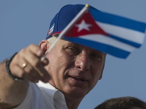 FILE - In this May 1, 2018 file photo, Cuba's President Miguel Diaz-Canel holds a national flag while watching the May Day parade file past at Revolution Square, in Havana, Cuba. A month after taking office, the Castros' successor as president of Cuba has broken from the immediate past, and made clear to Cubans that he will be operating far more like a conventional modern politician than the spotlight-shy general who selected him.