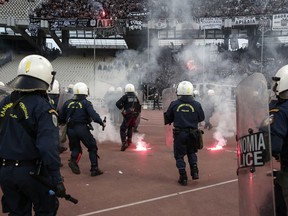 Greek policemen try to avoid flares thrown at them by fans ahead of a Greek Cup final in Athens' Olympic stadium in Athens, Saturday, May 12, 2018.