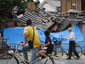 People pause to look at a collapsed house following an earthquake in Ibaraki City, north of Osaka prefecture on June 18, 2018.