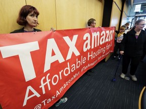 Demonstrators opposing the repeal of a tax on large companies such as Amazon and Starbucks that was intended to combat a growing homelessness crisis hold a sign that reads "Tax Amazon" as they wait for the start of a Seattle City Council meeting, Tuesday, June 12, 2018, at City Hall in Seattle.
