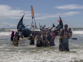 FILE - In this Sept. 14, 2017 file photo, a Rohingya man carries two children to shore in Shah Porir Dwip, Bangladesh, after they arrived on a boat from Myanmar. The U.N. refugee agency says nearly 69 million people who have fled war, violence and persecution were forcibly displaced last year, a new record for the fifth straight year. The U.N. High Commissioner for Refugees said Tuesday, June 19, 2018 that continued crises in places like South Sudan and Congo, as well as the exodus of Muslim Rohingya from Myanmar starting last year, raised the overall figure of forced displacements in 2017 to 68.5 million.