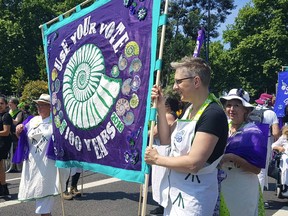 Participants hold up a banner as thousands of people march through the streets to celebrate 100 years since women were granted the vote, in London, Sunday June 10, 2018. Thousands of women gathered Sunday to turn British cities into rivers of green, white and violet to mark 100 years since the first U.K. women won the right to vote. Part artwork, part parade, "Processions" will see women march through London, Edinburgh, Cardiff and Belfast clad in the colors of the suffragette movement that fought for women's right to vote.