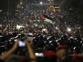 Jordanian protesters shout slogans and raise a national flag during a demonstration outside the Prime Minister's office in the capital Amman early Monday, June 4, 2018.  Thousands of Jordanians protested against a planned tax increase for a fourth straight day Sunday, marching toward the office of the prime minister and demanding his resignation.
