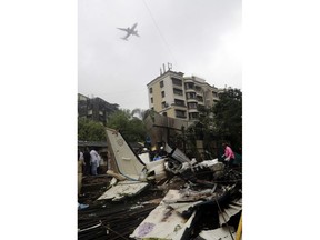 In this Thursday, June 28, 2018, file photo, an aircraft flies above as rescuers stand amid the wreckage of a private chartered plane that crashed in Ghatkopar area, Mumbai, India. The plane hit an open area at a construction site for a multistory building in a crowded area with many residential apartments.