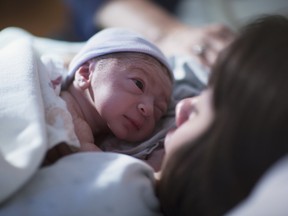 A newborn mixed race asian caucasian in a blue cap baby rest on his brunette asian mothers chest and stares into her eyes for the first time