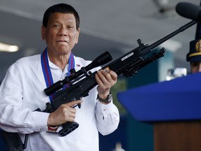 FILE - In this Thursday, April 19, 2018, file photo, Philippine President Rodrigo Duterte jokes to photographers as he holds an Israeli-made Galil rifle at Camp Crame in suburban Quezon city northeast of Manila, Philippines. The author of the first biography of Rodrigo Duterte says the maverick Philippine president is gravitating toward China partly because of a personal animosity toward the United States and its criticism of his human rights record.