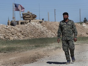 FILE - In this April 4, 2018 file photo, a U.S-backed Syrian Manbij Military Council soldier passes a U.S. position near the tense front line with Turkish-backed fighters, in Manbij, north Syria. The People's Protection Units, known by their Kurdish acronym YPG, said in a statement Tuesday, June 5, 2018, that it's pulling out of the key northern Syrian town of Manbij, potentially easing a serious rift between the United States and Turkey.