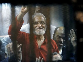 FILE - In this file photo dated Saturday, May 16, 2015, Muslim Brotherhood spiritual leader, Mohammed Badie wearing a red jumpsuit that designates he has been sentenced to death, waves from a defendants cage in a makeshift courtroom at the national police academy, in eastern Cairo, Egypt. It is announced Saturday June 30, 2018, that an Egyptian court has postponed until July 28 the verdicts for more than 700 defendants detained for their involvement in a 2013 sit-in, including Mohammed Badie.