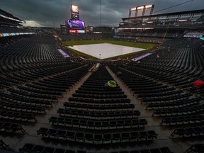 A few fans sit under umbrellas in the rain during a delayed baseball game between the Colorado Rockies and the New York Mets, Tuesday, June 19, 2018, in Denver.