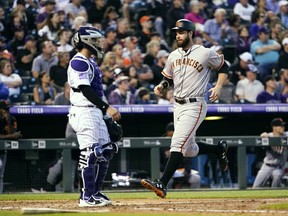 San Francisco Giants' Brandon Belt crosses home plate to score a run against the Colorado Rockies during the fifth inning of a baseball game as Rockies catcher Tony Wolters stands near the plate, Wednesday, May 30, 2018, in Denver.