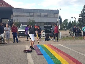A volunteer helps paint the colourful crosswalk in front of the Samson Cree Nation administration building to celebrate Pride Month in this image provided by the Maskwacis Community. A rainbow crosswalk in an Indigenous community south of Edmonton might be the first one on a First Nation reserve in Canada.