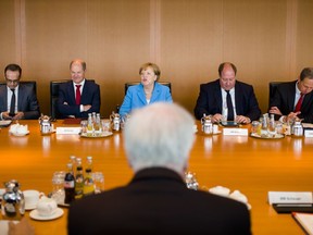 File - In this Wednesday, June 13, 2018 photo, German Interior Minister Horst Seehofer, front, sits on the opposite of German German Chancellor Angela Merkel, center back ground, prior to the weekly cabinet meeting of the German government at the chancellery in Berlin.