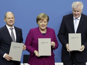 FILE - In this Monday, March 12, 2018 file photo, from left, Olaf Scholz, acting chairman of the German Social Democratic Party (SPD), German Chancellor and chairwomen of the German Christian Democratic Union (CDU), Angela Merkel, and the chairman of the German Christian Social Union (CSU), Horst Seehofer, pose with the coalition agreement during a signing ceremony in Berlin, Germany.