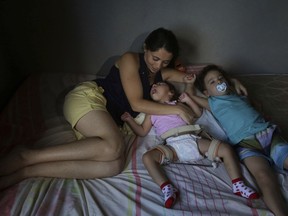In this May 4, 2018 photo, Cassiana Severina da Silva, lies on a bed with her 2-year-old twins, Melissa Vitoria, who was born with the Zika-caused microcephaly birth defect, and Edson Junior, at their home in Sao Lourenco da Mata, Brazil. "It was a shock for me. I had no idea this was even possible" to have one healthy twin and the other with microcephaly, said Severina.