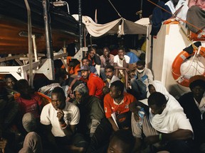 Rescued migrants sit in the search and rescue ship of German aid group Mission Lifeline as the boat remained stranded off Malta with 234 migrants aboard and no port at which to dock after both Italy and Malta refused to give authorization, early Monday, June 25, 2018.