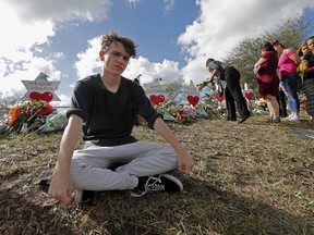 FILE- In this Feb. 19, 2018, file photo, Chris Grady, a student at Marjory Stoneman Douglas High School, sits at a memorial  in Parkland, Fla., for those slain in the Feb. 14 school shooting. Grady who had planned to join the U.S. Army before the shooting, has withdrawn his enlistment and will now work for the March for Our Lives movement.