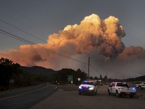 In this photo taken Thursday, May 31, 2018 and provided by Taosnews.com, officials confer as smoke rises from the Ute Park Fire in Ute Park, N.M. Evacuation centers have been set up in northeastern New Mexico as heavy smoke from a wildfire has forced residents from Cimarron and the surrounding areas to leave their homes. Authorities were directing people to the communities of Springer and Raton as conditions were expected to worsen Friday, June 1, 2018.
